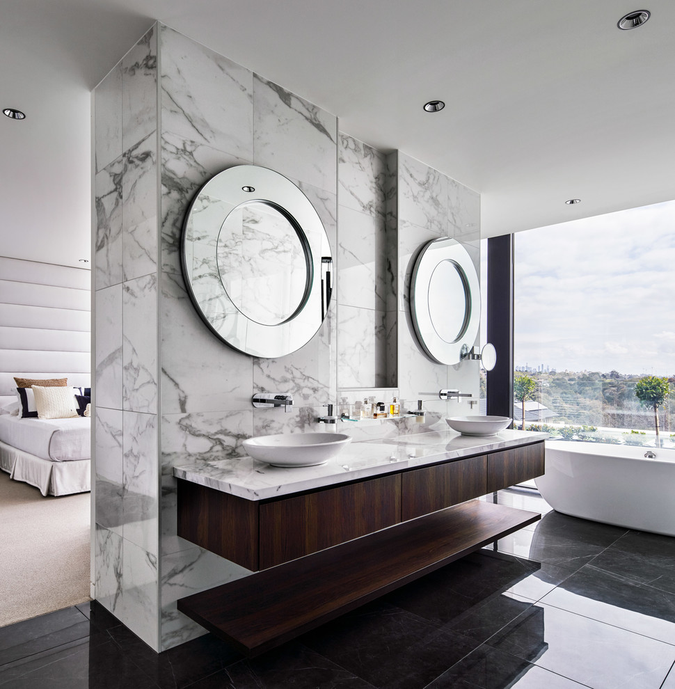 Inspiration for a large contemporary master bathroom in Melbourne with dark wood cabinets, a freestanding tub, white tile, marble, white walls, porcelain floors, marble benchtops, white benchtops, flat-panel cabinets, a vessel sink and black floor.