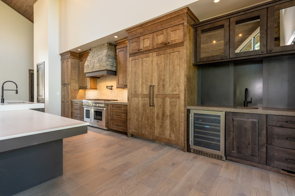 Inspiration for a large transitional single-wall open plan kitchen in Phoenix with an undermount sink, recessed-panel cabinets, brown cabinets, quartz benchtops, white splashback, stainless steel appliances, laminate floors, with island, brown floor and white benchtop.