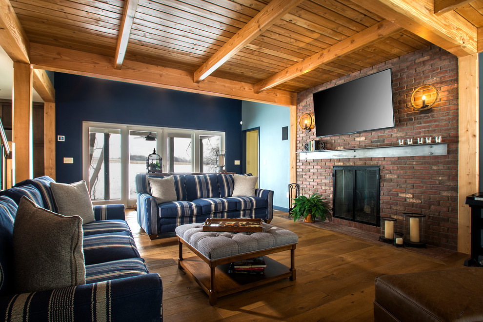 Photo of a country family room in New York with medium hardwood floors, a brick fireplace surround, brown floor, blue walls, a standard fireplace and a wall-mounted tv.