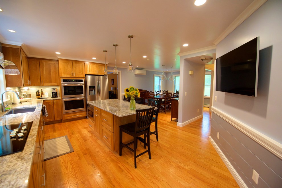 This is an example of a large traditional l-shaped eat-in kitchen in Providence with a single-bowl sink, granite benchtops, glass tile splashback, stainless steel appliances, with island, shaker cabinets, light wood cabinets, grey splashback, light hardwood floors, brown floor and grey benchtop.