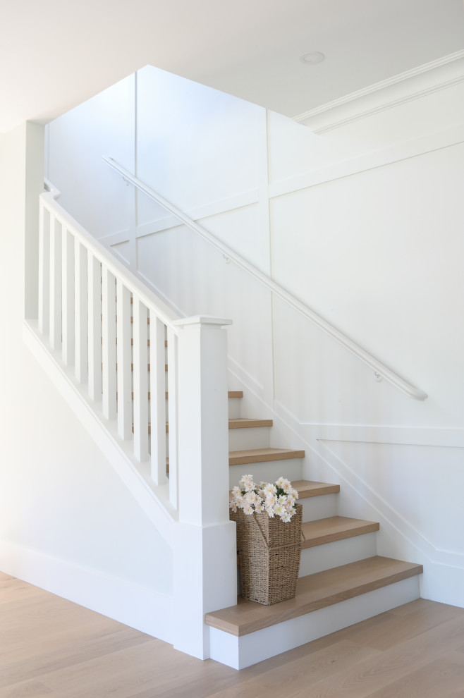 На фото: прямая лестница среднего размера в стиле неоклассика (современная классика) с деревянными ступенями, крашенными деревянными подступенками, деревянными перилами и панелями на части стены