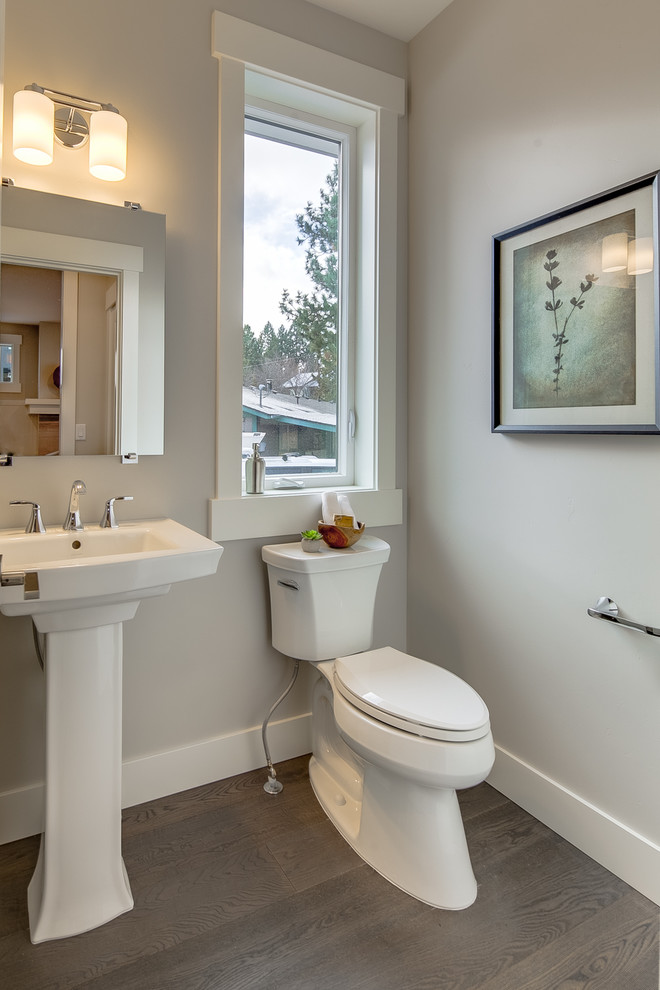 Photo of a small transitional powder room in Other with a two-piece toilet, beige walls, dark hardwood floors, a pedestal sink, solid surface benchtops, brown floor and white benchtops.
