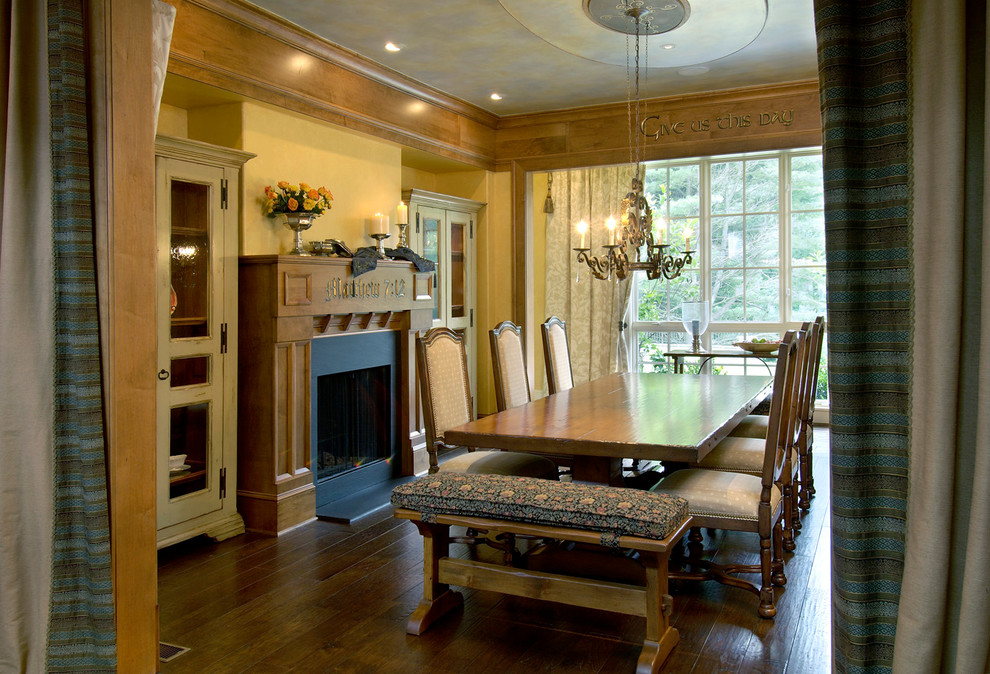 Example of a mid-sized transitional medium tone wood floor enclosed dining room design with yellow walls, a standard fireplace and a wood fireplace surround