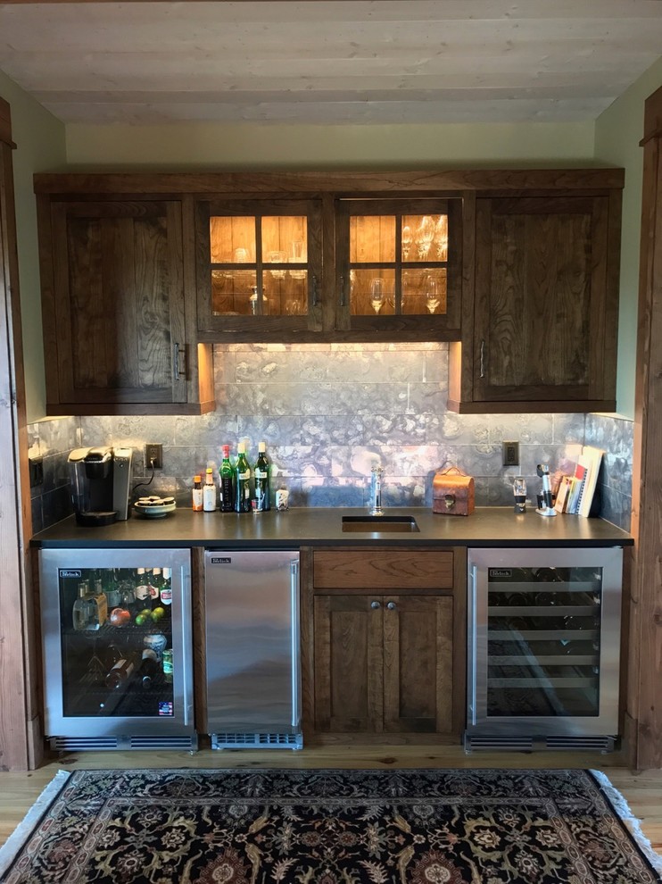 This is an example of a mid-sized country single-wall wet bar in Other with an undermount sink, shaker cabinets, dark wood cabinets, solid surface benchtops, grey splashback, metal splashback, light hardwood floors and beige floor.