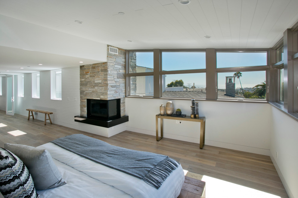 Design ideas for a large contemporary master bedroom in Los Angeles with white walls, light hardwood floors, a corner fireplace and a stone fireplace surround.