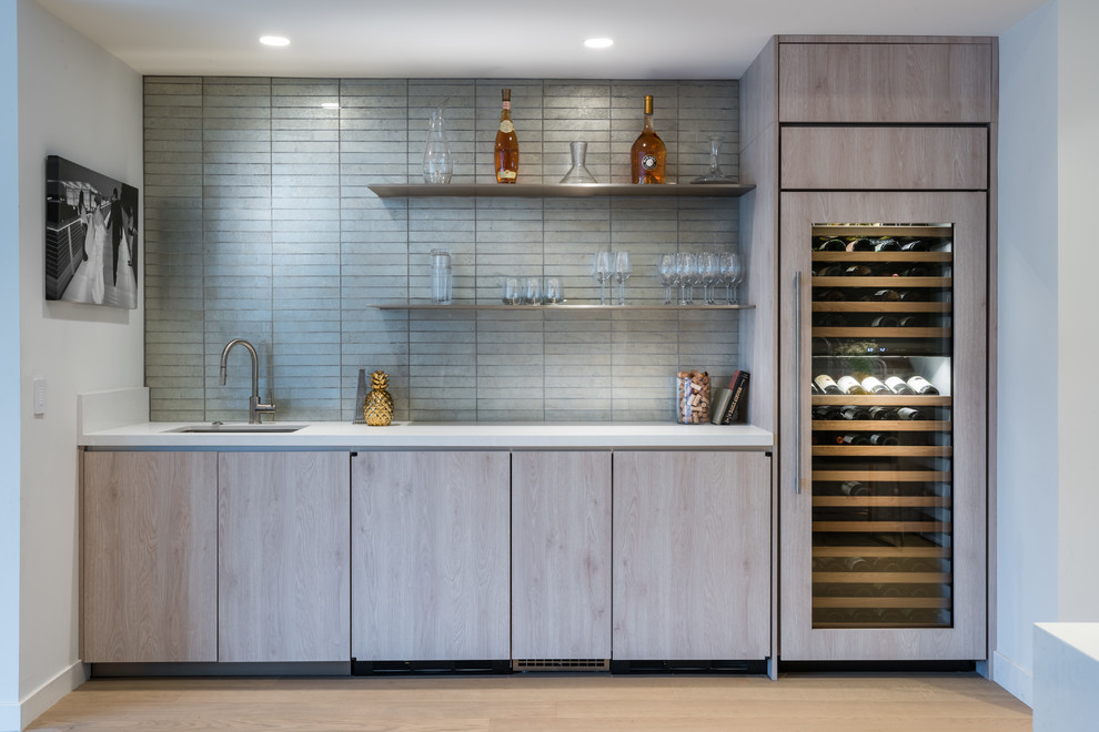 This is an example of a contemporary single-wall wet bar in Los Angeles with an undermount sink, flat-panel cabinets, white benchtop, light hardwood floors, medium wood cabinets, grey splashback, subway tile splashback and beige floor.