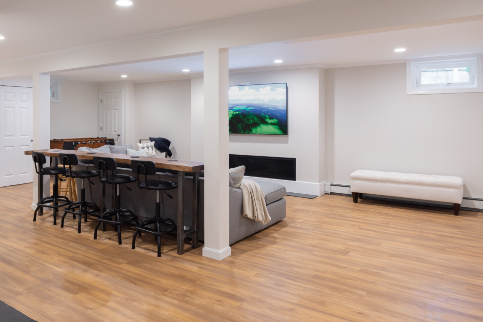 Medium sized modern basement in Boston with a home bar, grey walls, vinyl flooring, a ribbon fireplace and brown floors.