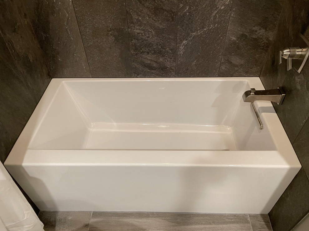 Bild på ett mellanstort funkis svart svart badrum för barn, med luckor med infälld panel, vita skåp, ett badkar i en alkov, en dusch/badkar-kombination, en toalettstol med separat cisternkåpa, brun kakel, porslinskakel, grå väggar, klinkergolv i porslin, ett undermonterad handfat, granitbänkskiva, grått golv och dusch med duschdraperi