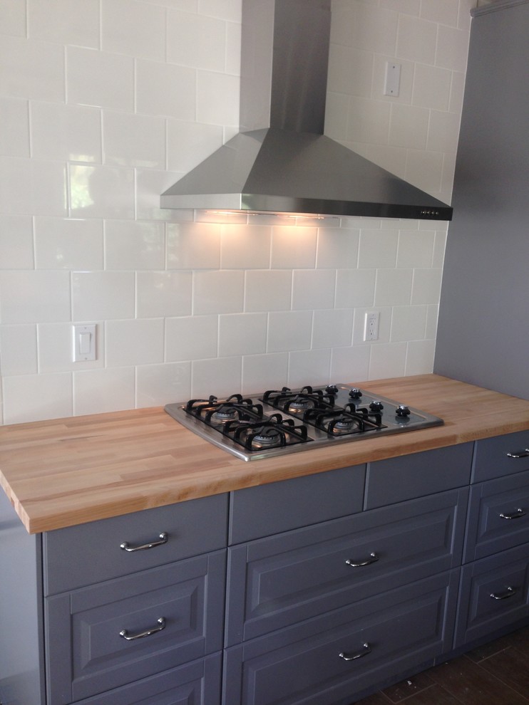 Transitional u-shaped laminate floor and brown floor enclosed kitchen photo with a farmhouse sink, shaker cabinets, blue cabinets, wood countertops, white backsplash, subway tile backsplash, stainless steel appliances and brown countertops