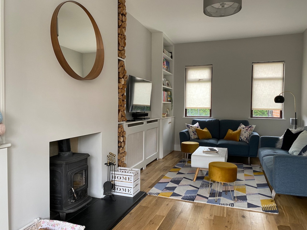 This is an example of a mid-sized scandinavian living room in Belfast with grey walls, light hardwood floors, a wood stove and a built-in media wall.