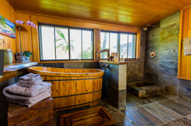 This is an example of a mid-sized tropical master bathroom in Hawaii with open cabinets, medium wood cabinets, a japanese tub, an open shower, gray tile, pebble tile, grey walls, slate floors, a vessel sink, wood benchtops, grey floor and an open shower.
