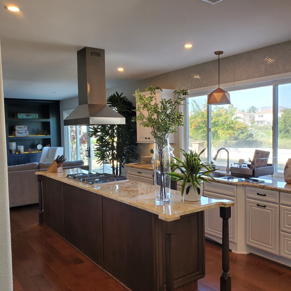 Inspiration for a transitional kitchen in San Diego with a double-bowl sink, raised-panel cabinets, white cabinets, granite benchtops, beige splashback, mosaic tile splashback, stainless steel appliances, plywood floors, with island, brown floor and yellow benchtop.