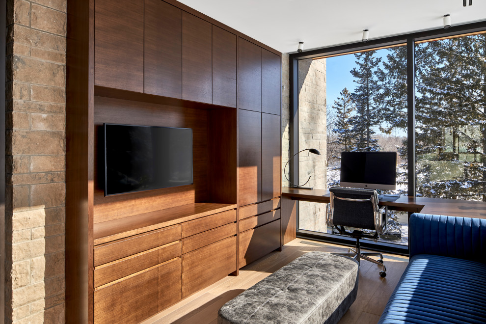 Cette photo montre une petite salle de séjour tendance fermée avec un mur beige, un sol en bois brun, un téléviseur encastré, un sol beige et un mur en parement de brique.