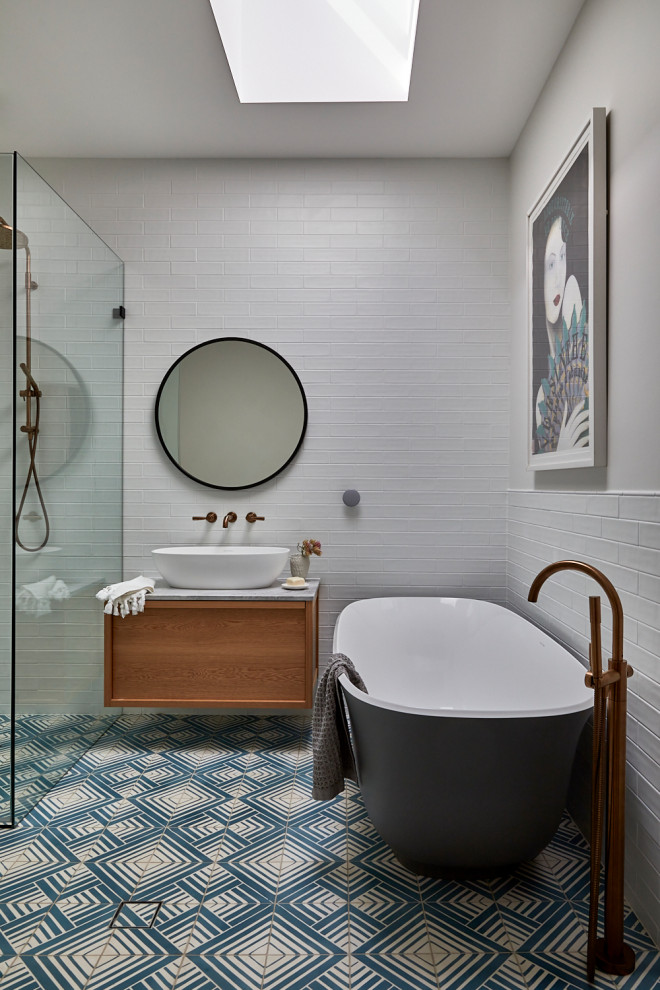 Mid-sized beach style master bathroom in Sydney with furniture-like cabinets, medium wood cabinets, a freestanding tub, an open shower, a wall-mount toilet, white tile, subway tile, white walls, cement tiles, a vessel sink, marble benchtops, blue floor, a hinged shower door, grey benchtops, a laundry, a single vanity, a floating vanity, recessed and brick walls.