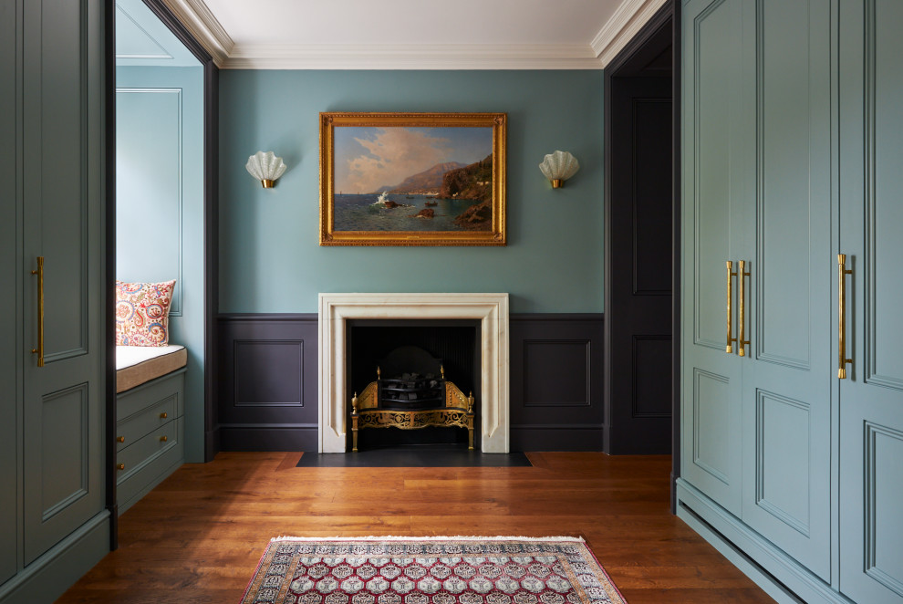 This is an example of a mid-sized traditional gender-neutral walk-in wardrobe in London with recessed-panel cabinets, blue cabinets, medium hardwood floors, brown floor and coffered.