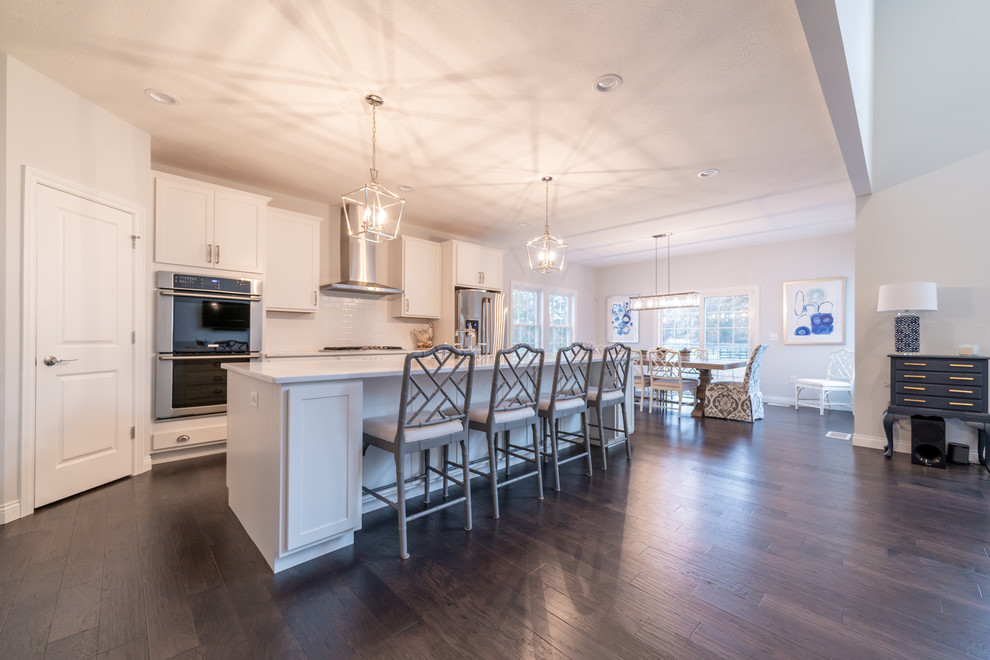 Inspiration for a transitional galley dark wood floor and brown floor open concept kitchen remodel in Cleveland with shaker cabinets, white cabinets, white backsplash, stainless steel appliances, an island and white countertops