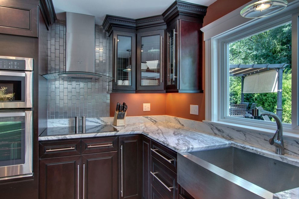 Mid-sized transitional l-shaped medium tone wood floor and brown floor eat-in kitchen photo in Raleigh with a farmhouse sink, raised-panel cabinets, dark wood cabinets, marble countertops, stainless steel appliances, an island and white countertops