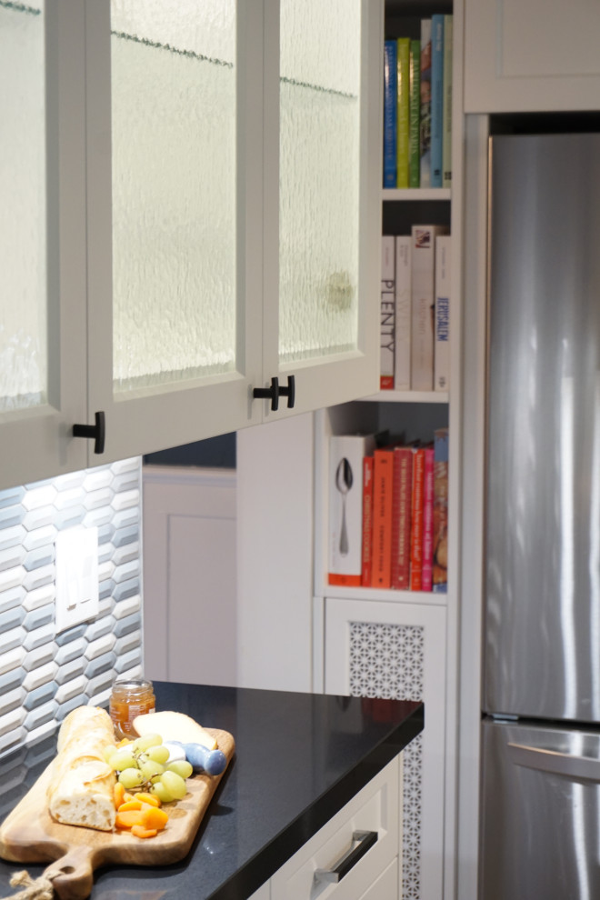 Example of a mid-sized transitional galley light wood floor and gray floor kitchen design in Toronto with an undermount sink, glass-front cabinets, white cabinets, quartz countertops, blue backsplash, ceramic backsplash, stainless steel appliances and black countertops