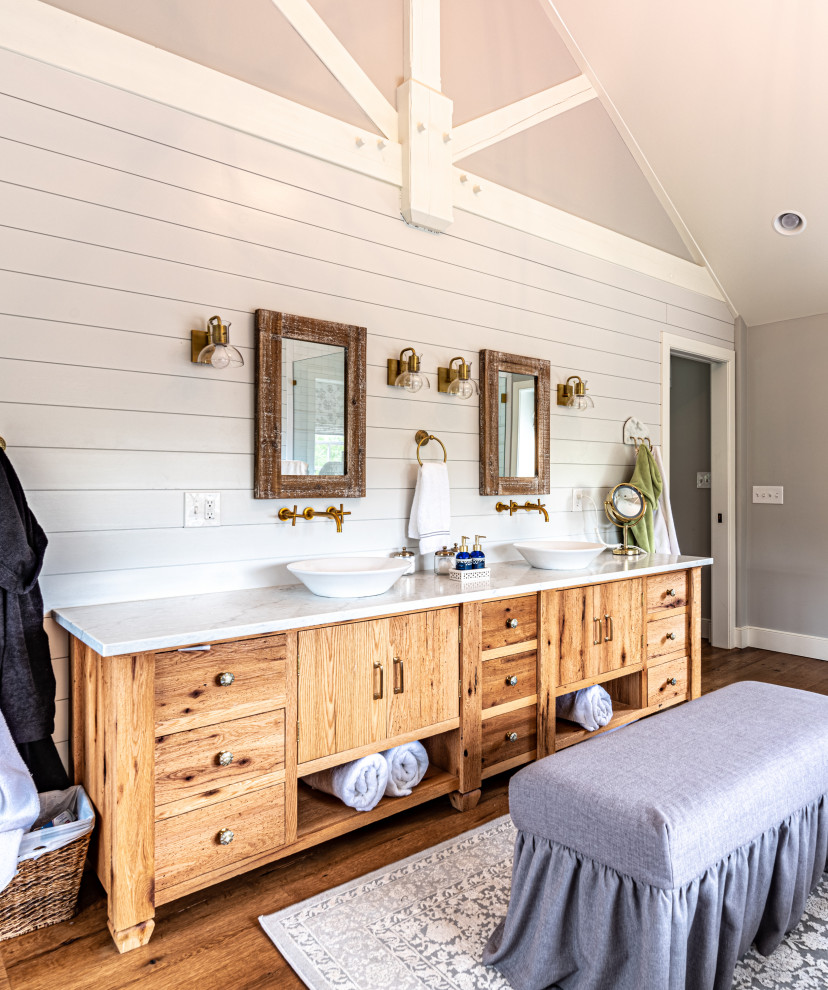 This is an example of a mid-sized country master bathroom in Philadelphia with furniture-like cabinets, distressed cabinets, a corner shower, a bidet, white walls, light hardwood floors, a vessel sink, engineered quartz benchtops, a hinged shower door and white benchtops.