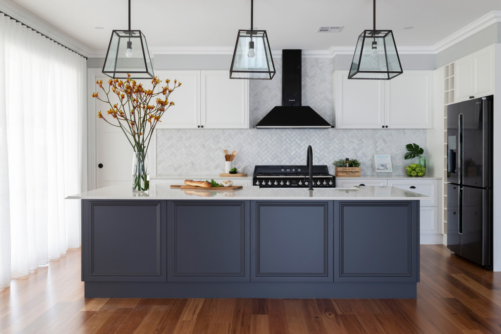 This is an example of a mid-sized traditional galley open plan kitchen in Canberra - Queanbeyan with a farmhouse sink, shaker cabinets, blue cabinets, quartz benchtops, white splashback, mosaic tile splashback, black appliances, light hardwood floors, multiple islands and white benchtop.