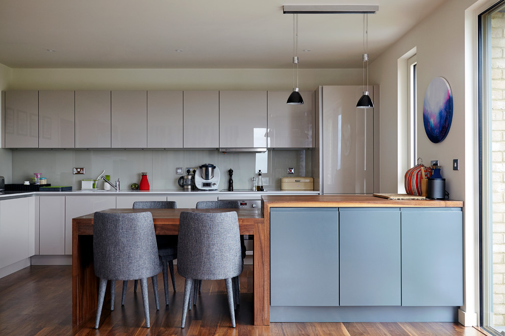 Design ideas for a mid-sized contemporary l-shaped open plan kitchen in London with a drop-in sink, flat-panel cabinets, grey cabinets, grey splashback, glass sheet splashback, stainless steel appliances, dark hardwood floors and with island.
