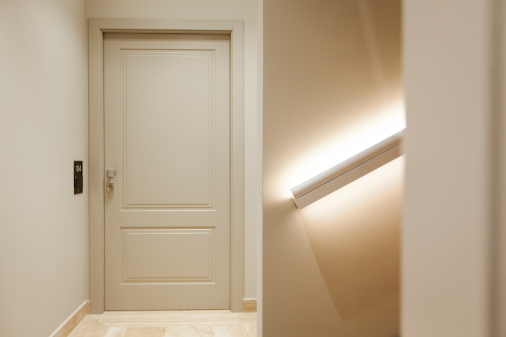Réalisation d'un grand couloir minimaliste avec un mur beige, un sol en marbre, un sol beige et un plafond décaissé.