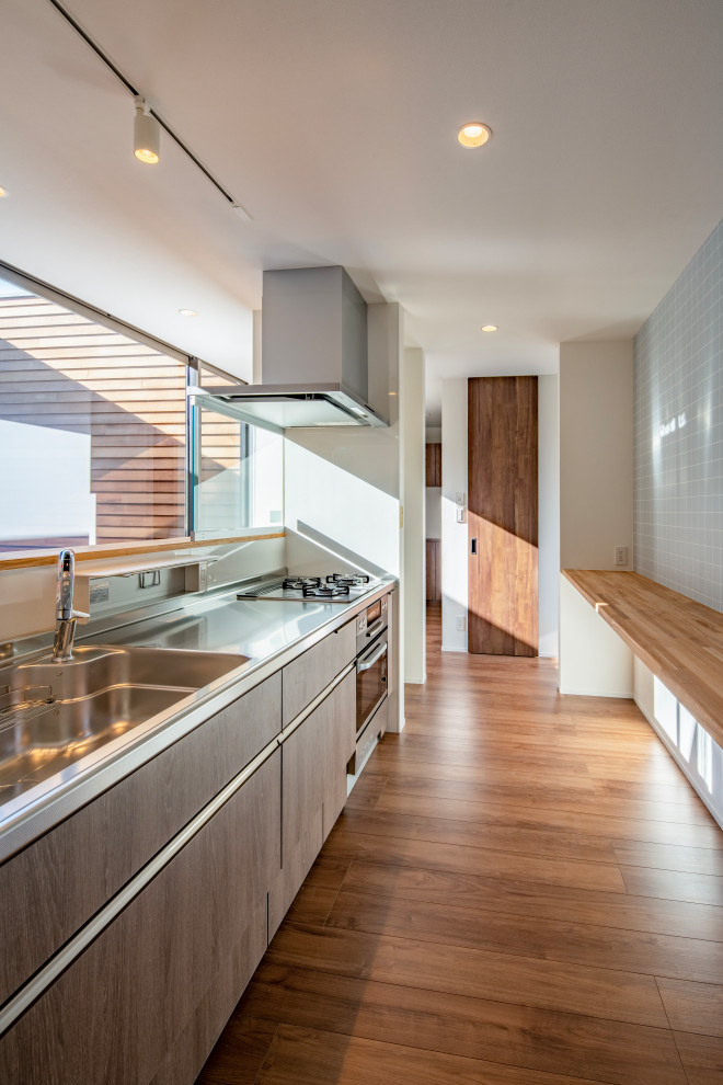Medium sized contemporary grey and brown single-wall open plan kitchen in Other with an integrated sink, medium wood cabinets, stainless steel worktops, brown splashback, plywood flooring, an island, brown floors and a wallpapered ceiling.