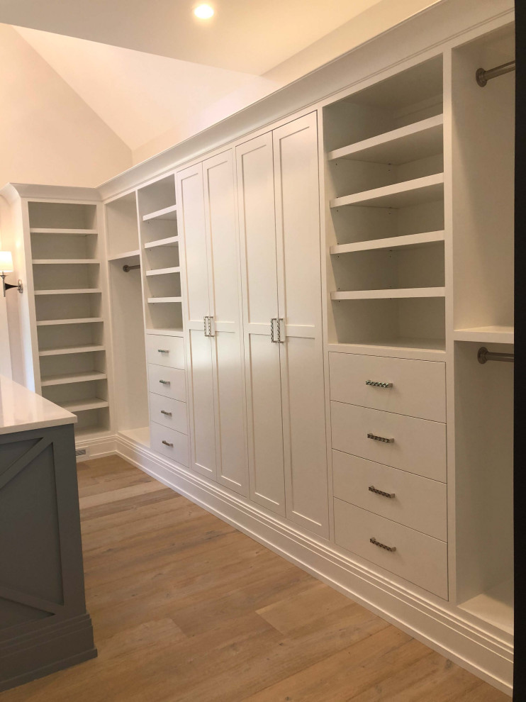 Design ideas for a large gender-neutral walk-in wardrobe in Detroit with white cabinets, light hardwood floors and exposed beam.