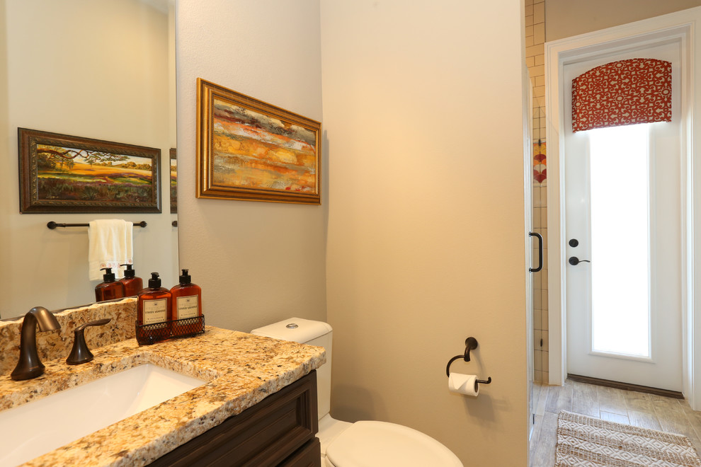 This is an example of a mid-sized beach style bathroom in Orlando with raised-panel cabinets, brown cabinets, an alcove shower, a two-piece toilet, beige tile, ceramic tile, beige walls, porcelain floors, an undermount sink, granite benchtops, beige floor and a hinged shower door.