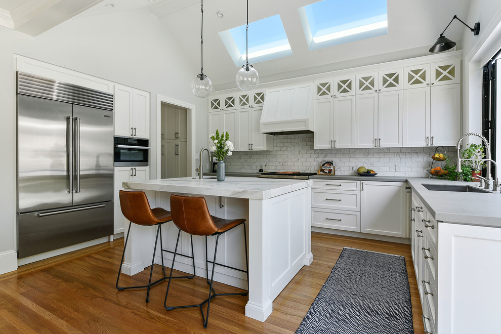 Mid-sized midcentury u-shaped separate kitchen in San Francisco with an undermount sink, shaker cabinets, white cabinets, concrete benchtops, white splashback, marble splashback, stainless steel appliances, medium hardwood floors, with island, brown floor and grey benchtop.