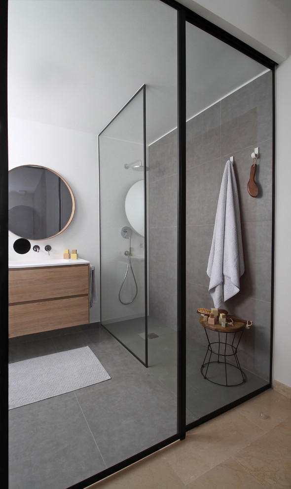 Photo of a mid-sized modern master bathroom in Valencia with flat-panel cabinets, medium wood cabinets, an open shower, a wall-mount toilet, gray tile, white walls, grey floor, white benchtops and a console sink.