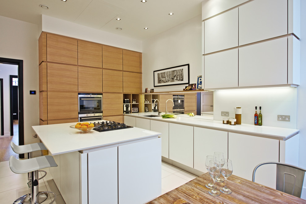 Mid-sized contemporary galley eat-in kitchen in London with flat-panel cabinets, white cabinets, white splashback, stainless steel appliances, ceramic floors, with island, an undermount sink, solid surface benchtops, mirror splashback, white floor and white benchtop.