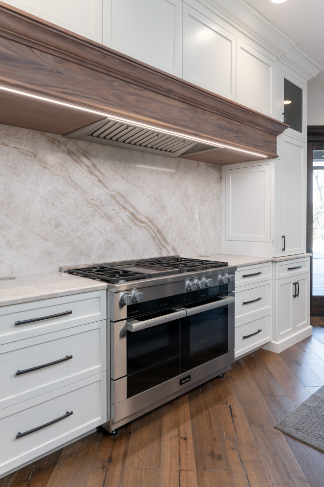 Inspiration for a large transitional medium tone wood floor and brown floor open concept kitchen remodel with a double-bowl sink, flat-panel cabinets, white cabinets, quartzite countertops, beige backsplash, stainless steel appliances, an island and beige countertops