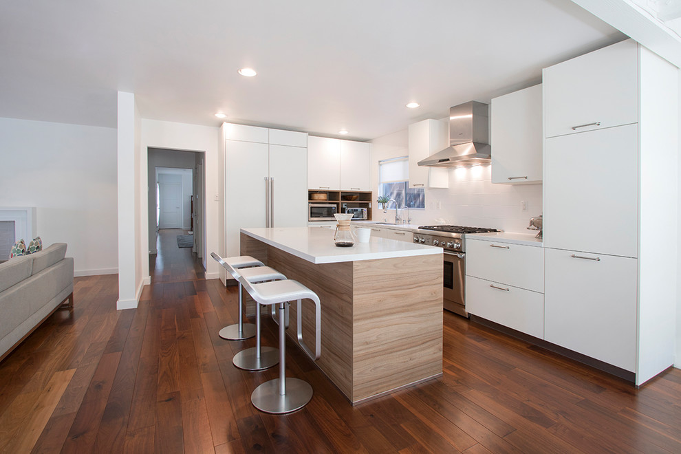 Mid-sized contemporary l-shaped eat-in kitchen in Los Angeles with a drop-in sink, flat-panel cabinets, medium wood cabinets, quartzite benchtops, white splashback, porcelain splashback, stainless steel appliances, laminate floors, with island, brown floor and white benchtop.