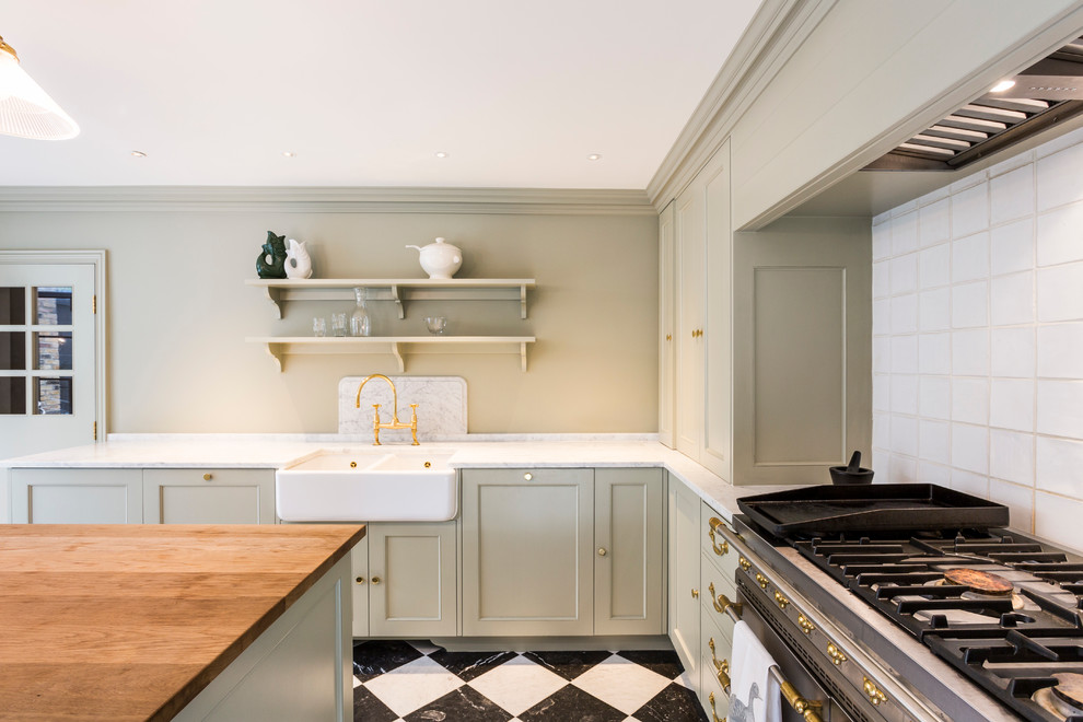 Inspiration for a traditional l-shaped open plan kitchen in London with a farmhouse sink, beaded inset cabinets, green cabinets, marble benchtops, white splashback, ceramic splashback, stainless steel appliances and with island.