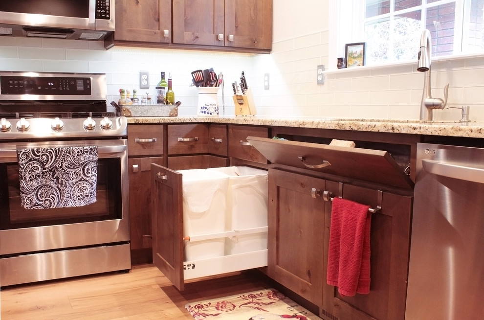 Example of a large mountain style u-shaped light wood floor and brown floor open concept kitchen design in Boise with an undermount sink, shaker cabinets, brown cabinets, granite countertops, white backsplash, glass tile backsplash, stainless steel appliances and an island