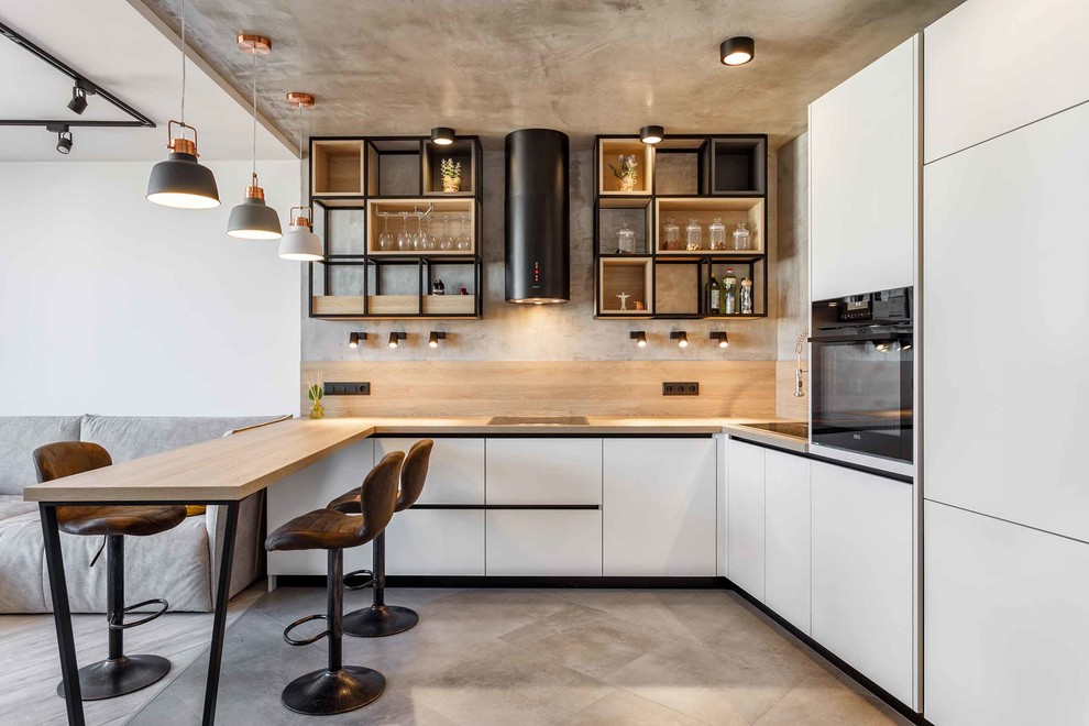 Photo of a contemporary u-shaped open plan kitchen in Other with a single-bowl sink, flat-panel cabinets, white cabinets, wood benchtops, beige splashback, window splashback, black appliances, concrete floors, a peninsula, grey floor and beige benchtop.