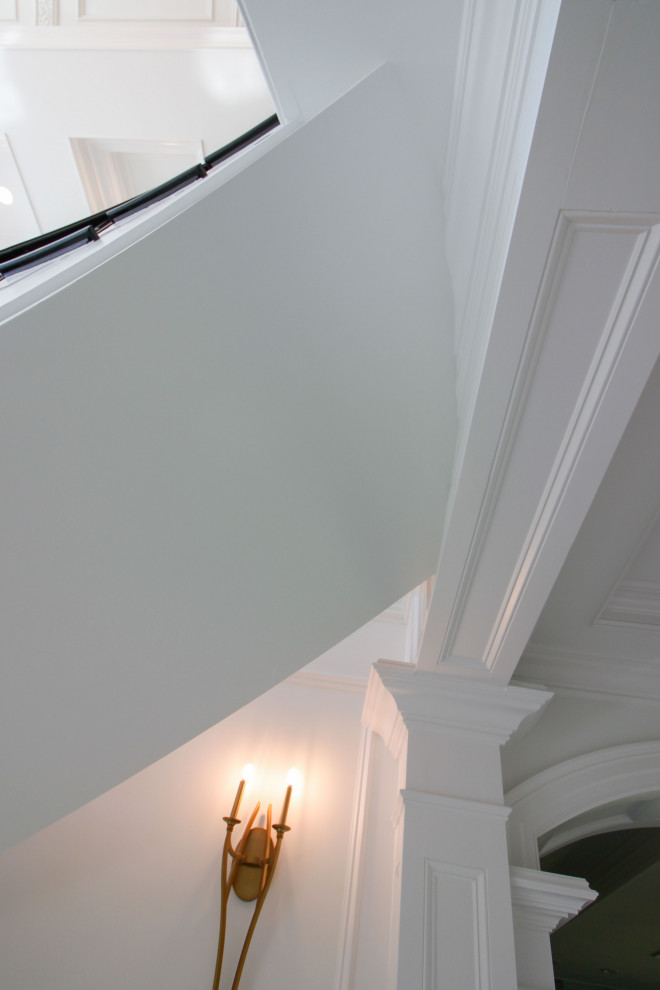 На фото: огромная изогнутая деревянная лестница в стиле неоклассика (современная классика) с деревянными ступенями, перилами из смешанных материалов и панелями на стенах