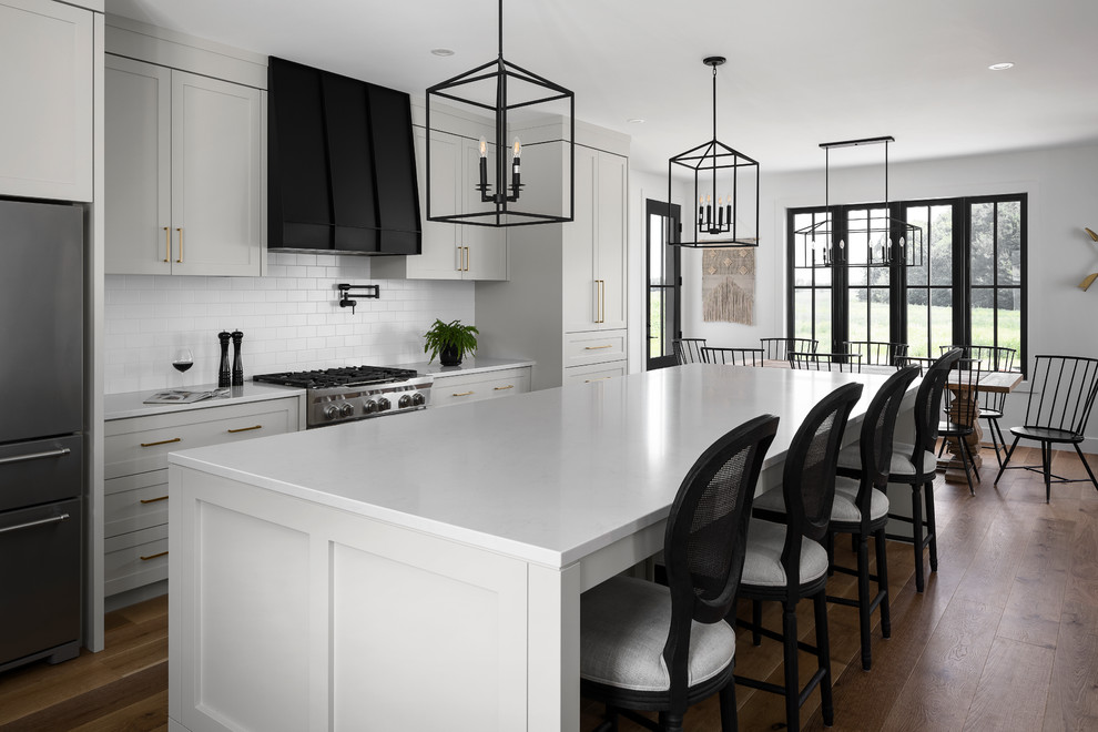Inspiration for a large country single-wall eat-in kitchen in Toronto with a farmhouse sink, shaker cabinets, grey cabinets, quartz benchtops, white splashback, subway tile splashback, stainless steel appliances, light hardwood floors, with island, brown floor and grey benchtop.