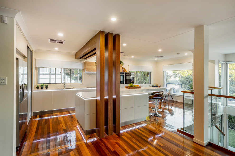 This is an example of a large contemporary l-shaped eat-in kitchen in Brisbane with an undermount sink, flat-panel cabinets, beige cabinets, quartz benchtops, white splashback, stone slab splashback, black appliances, medium hardwood floors, with island, multi-coloured floor and yellow benchtop.