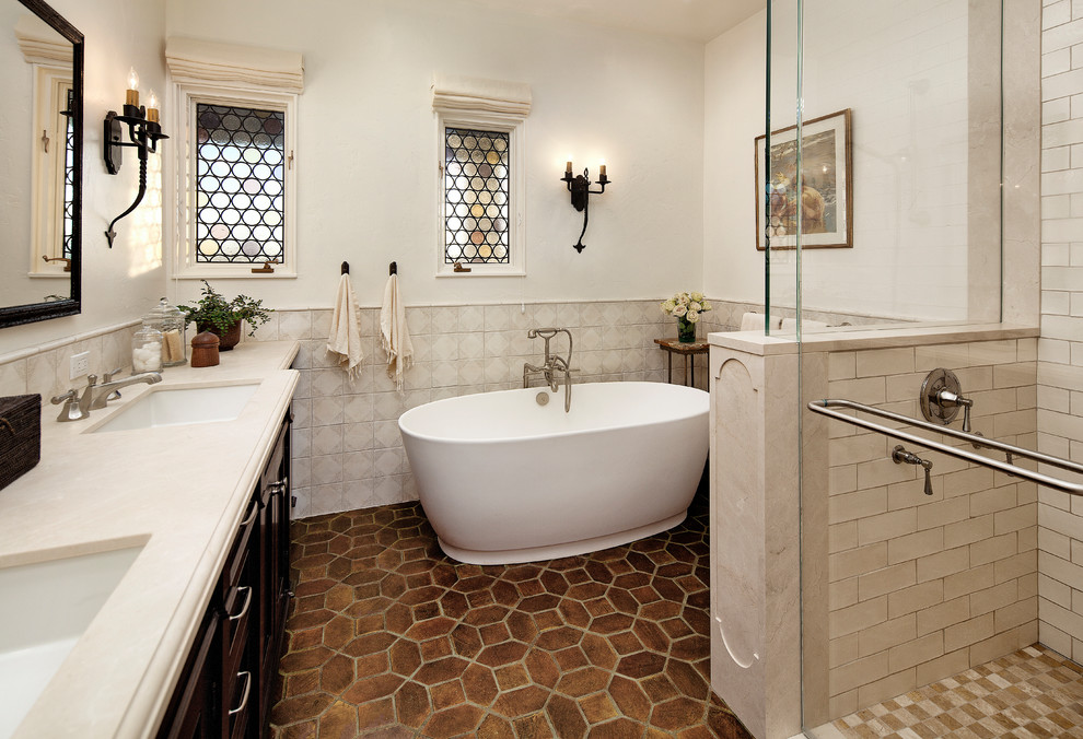 Photo of a small mediterranean master bathroom in Santa Barbara with recessed-panel cabinets, dark wood cabinets, a freestanding tub, an alcove shower, multi-coloured tile, ceramic tile, white walls, an undermount sink, solid surface benchtops, brown floor, a hinged shower door and terra-cotta floors.