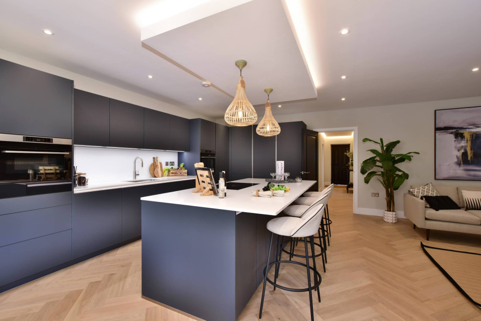 Example of a large trendy l-shaped open concept kitchen design in Hertfordshire with flat-panel cabinets, gray cabinets, quartzite countertops, white backsplash, black appliances, an island and white countertops