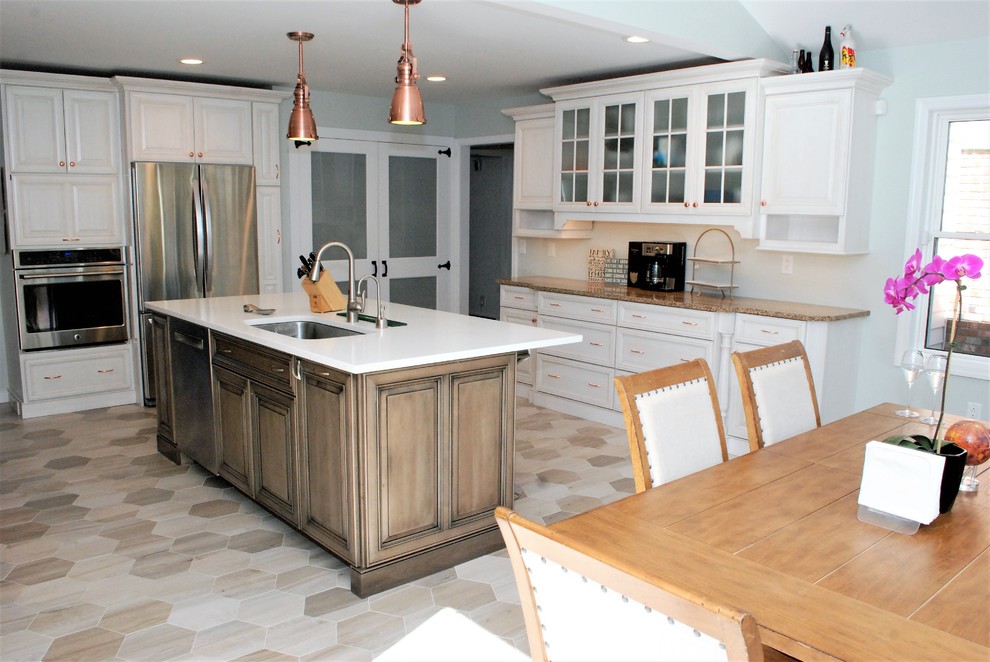 Example of a mid-sized transitional l-shaped porcelain tile and beige floor enclosed kitchen design in New York with an undermount sink, raised-panel cabinets, white cabinets, solid surface countertops, white backsplash, porcelain backsplash, stainless steel appliances and an island