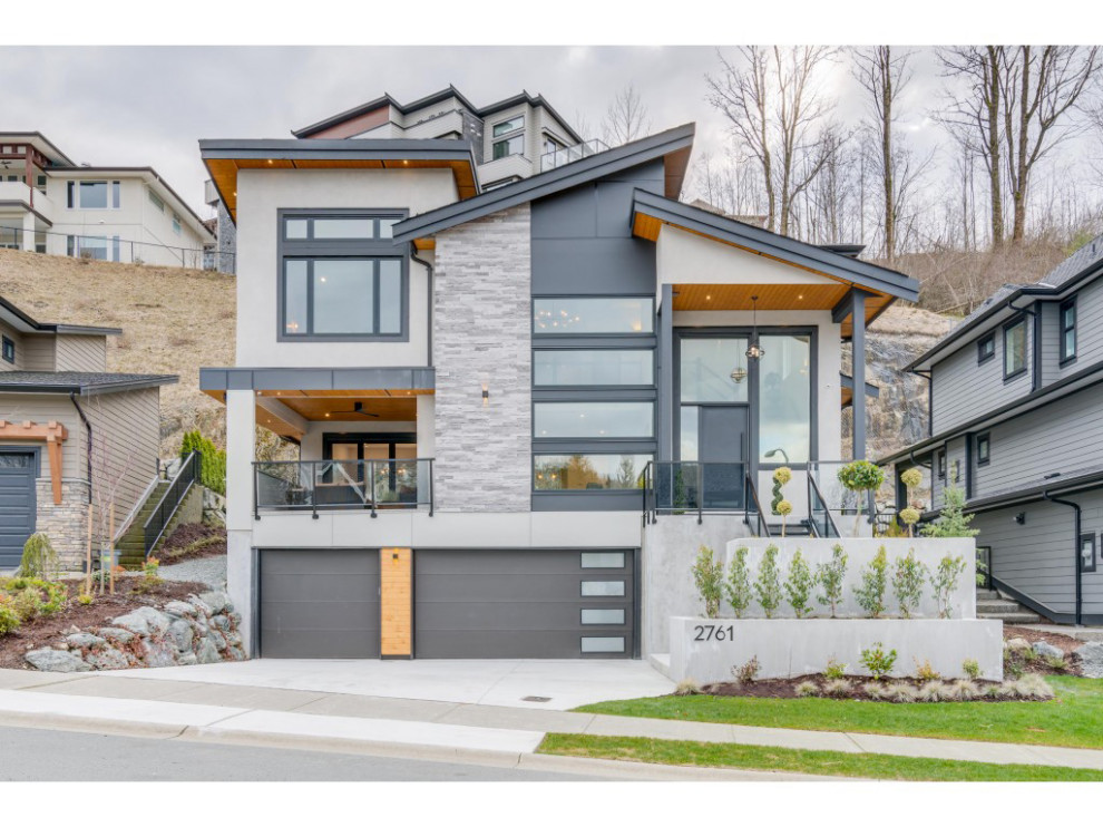 Photo of a large contemporary three-storey stucco grey house exterior in Vancouver with a shed roof and a shingle roof.