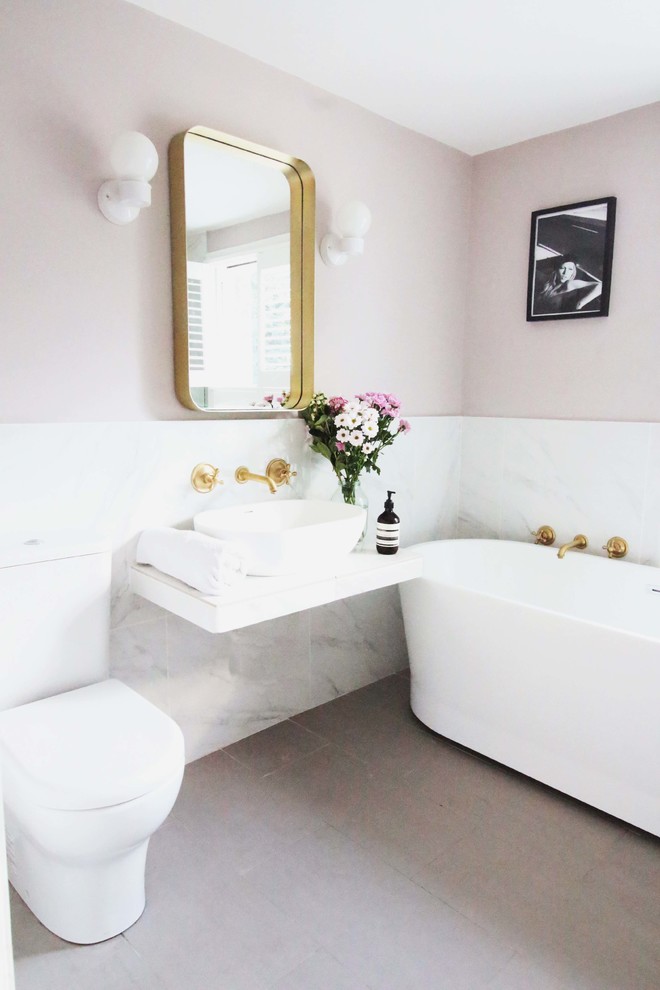 Photo of a mid-sized contemporary bathroom in London with a freestanding tub, a two-piece toilet, gray tile, white tile, marble, pink walls, a vessel sink and grey floor.