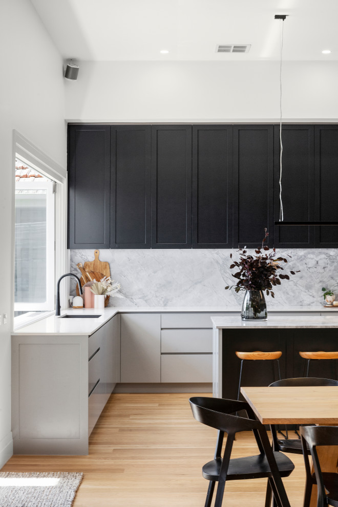 Inredning av ett modernt stort grå grått kök, med en dubbel diskho, skåp i shakerstil, marmorbänkskiva, grått stänkskydd, stänkskydd i marmor, svarta vitvaror, ljust trägolv och en köksö
