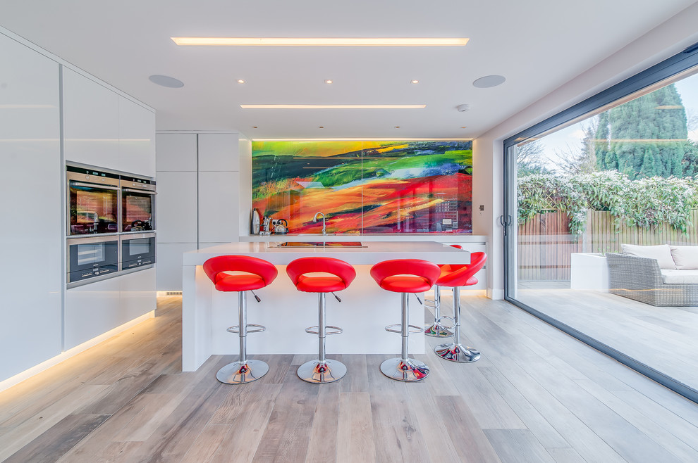 Inspiration for a mid-sized contemporary kitchen in Surrey with flat-panel cabinets, white cabinets, quartzite benchtops, multi-coloured splashback, glass sheet splashback, stainless steel appliances and with island.