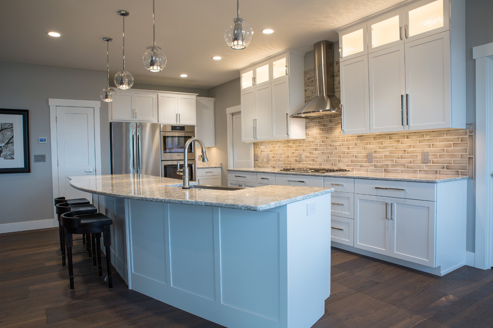 Inspiration for a large transitional l-shaped kitchen in Other with dark hardwood floors, a farmhouse sink, shaker cabinets, white cabinets, granite benchtops, grey splashback, stone tile splashback, stainless steel appliances and with island.