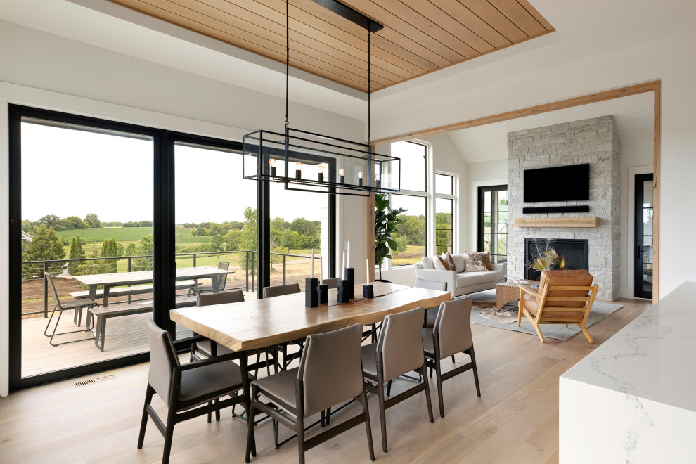 Photo of an expansive transitional kitchen/dining combo in Minneapolis with white walls, light hardwood floors, a two-sided fireplace, a stone fireplace surround and timber.