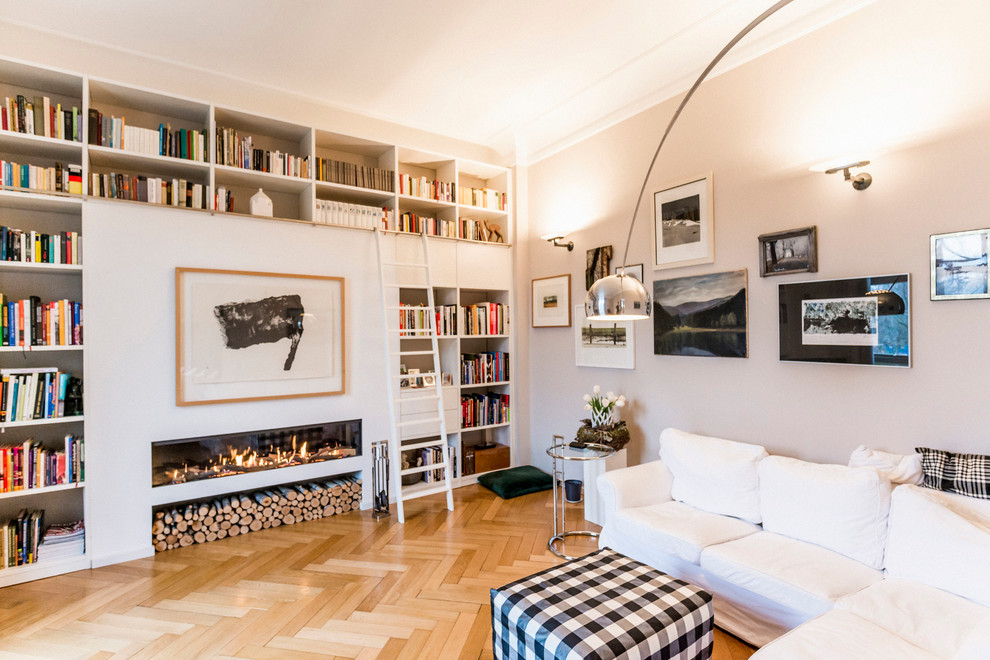 This is an example of a large contemporary living room in Berlin with a library, grey walls, light hardwood floors, a ribbon fireplace, a plaster fireplace surround and no tv.
